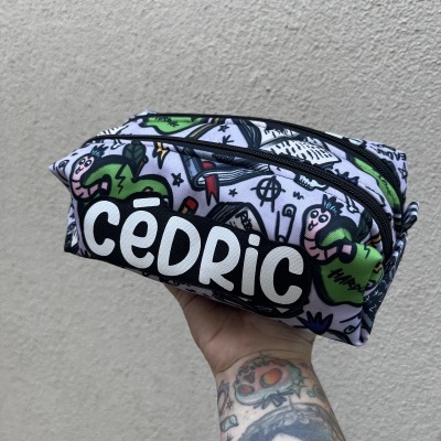 Bolsa com padrão colorido e o texto CÉDRIC em branco sobre fundo preto