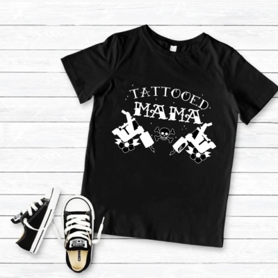 T-shirt preta com texto e desenhos brancos e ténis infantis pretos sobre fundo de madeira clara