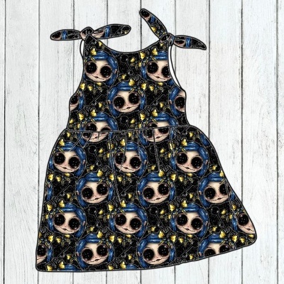 Vestido infantil com padrão colorido de rostos estilizados, alças em laço, em fundo branco de tábuas de madeira