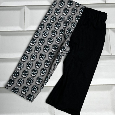 Calças infantis com perna preta e perna com padrão de caveiras sobre fundo branco de azulejos