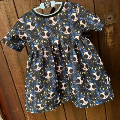 Vestido infantil colorido com padrão cartoon pendurado num cabide azul claro