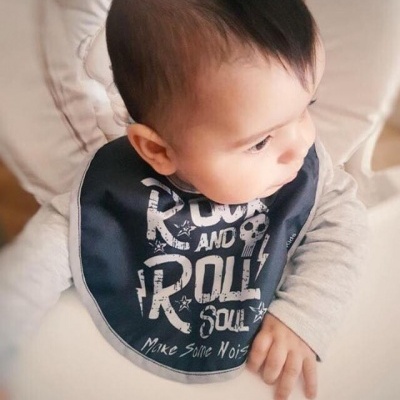 Bebé com babete preto e texto branco sentado numa cadeira alta