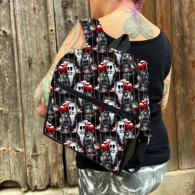 Mochila preta com padrão de caveiras e corações vermelhos fotografada numa pessoa junto a uma parede de madeira