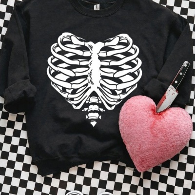 Sweatshirt preta com estampa de caixa torácica em forma de coração e peluche rosa em formato de coração com faca