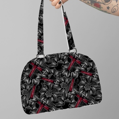 Mala preta com padrão vermelho e cinza, segurada por mão tatuada.