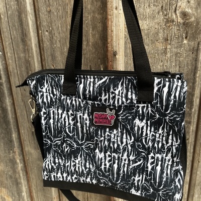 Mala preta e branca com padrão e etiqueta MOSHPIT MEMORIES pendurada em fundo de madeira