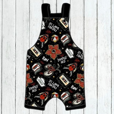 Macacão curto infantil preto com estampas coloridas variadas e textos em inglês.