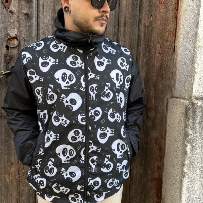 Casaco preto e branco com padrão de caveiras usado por homem junto a porta de madeira