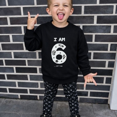 Criança a usar camisola preta com texto branco e calças pretas com padrão branco