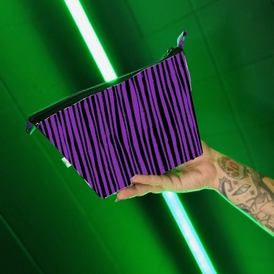 Bolsa roxa com riscas pretas segurada por uma mão tatuada com fundo verde