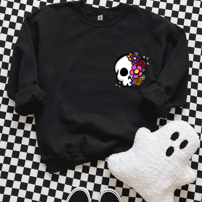 Sweatshirt preta com estampa de caveira flores coloridas, peluche fantasma branco, sapatilhas pretas sobre padrão quadriculado.