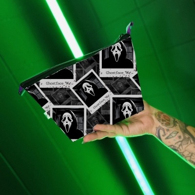 Necessaire preta com padrão Ghostface e texto 'Ghostface 96' e 'Scream' sendo segurada