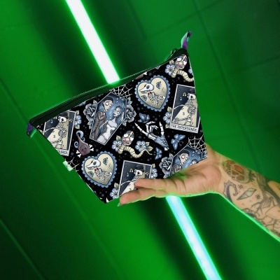 Bolsa pequena com padrão de tarô em fundo preto segurada por mão tatuada em ambiente iluminado por luz verde