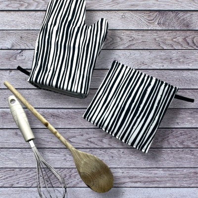 Luvas e descansos de panela com riscas preto e branco, batedor de metal e colher de pau sobre fundo de madeira