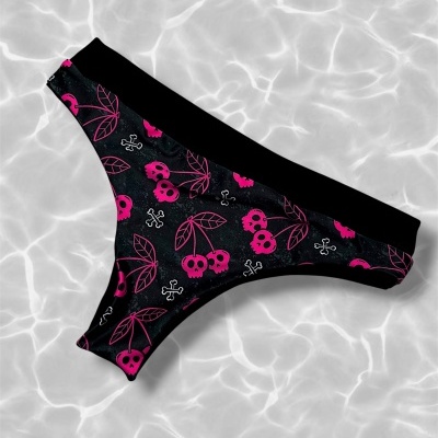 Parte de baixo de biquíni preto com estampado rosa de cerejas em forma de caveira e ossos, sobre fundo claro com reflexos de água.
