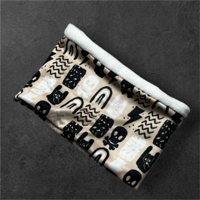 Cachecol tubular bege com padrão preto e branco com caveiras e gatos em fundo cinzento.