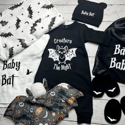 Roupas e acessórios para bebé com tema de morcego em cores preto, branco e cinzento, incluindo pijama, touca, sapatinhos, saco, manta e toalha