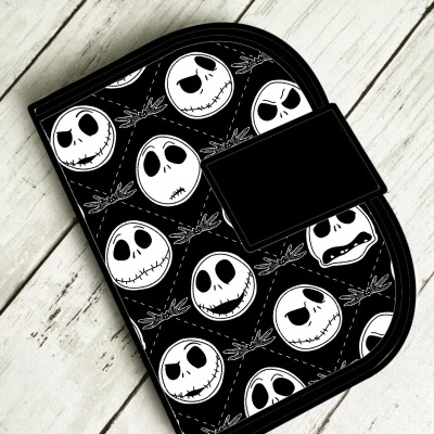 Bolsa preta com desenhos de caveiras brancas sobre madeira clara