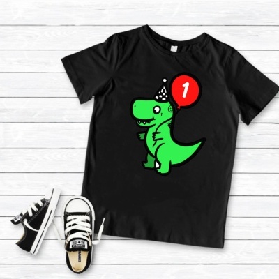 T-shirt preta com estampa de dinossauro verde a segurar balão vermelho com número 1 e sapatilhas pretas ao lado