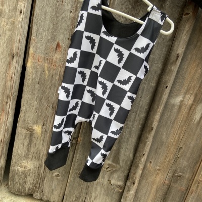 Macacão preto e branco com padrão de morcegos, pendurado em cabide branco, em porta de madeira.