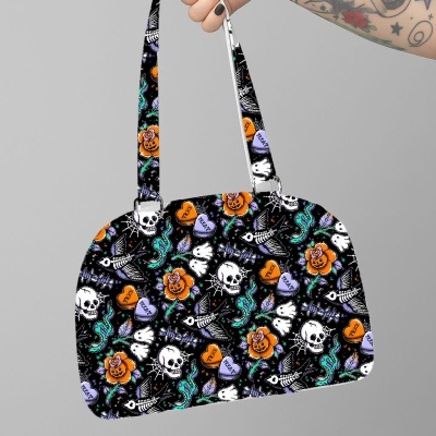 Mala de mão preta com padrão de caveiras, flores, peixes esqueleto, corações com texto e polvos, mão tatuada segurando.