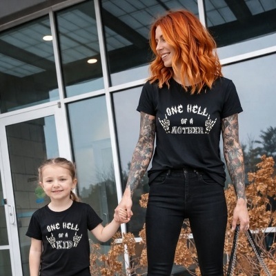 Duas pessoas com t-shirts pretas e textos brancos, à frente de um edifício com vidros grandes.