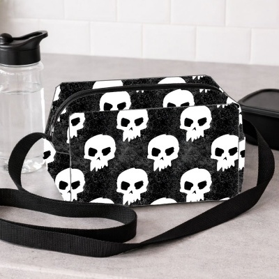 Bolsa tiracolo preta com padrão de caveiras brancas em bancada cinza