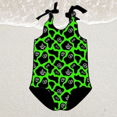 Fato de banho infantil verde com padrão de caveiras e ossos em areia à beira do mar
