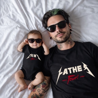 Pai e bebé deitados em cama branca com t-shirt e body pretos e texto FATHER Tour! e MINI tour!