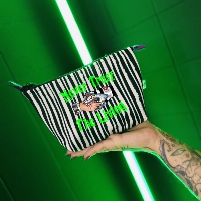 Bolsa pequena riscada preta e branca com texto 'Never Trust The Living' em verde, segurada por mão tatuada