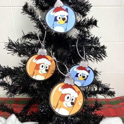 Ornamentos de Natal redondos com personagens de desenho animado pendurados numa árvore preta.