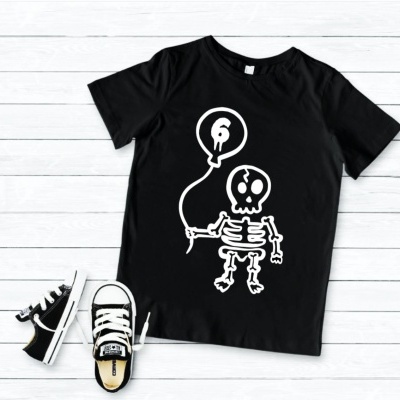 Camiseta preta com desenho de esqueleto e balão branco, e sapatilhas pretas e brancas, sobre fundo de madeira branca