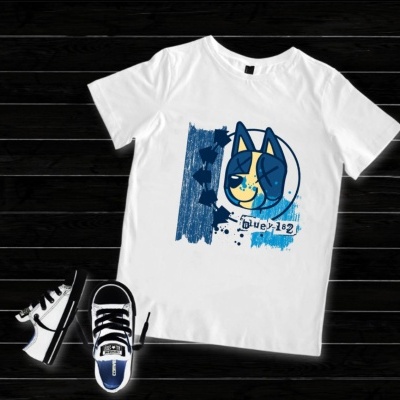 Camiseta branca com estampa de cão azul e amarelo, sapatos desportivos brancos e pretos sobre chão de madeira escura