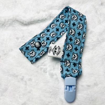 Prendedor de chupeta azul com caveiras brancas e cruzes pretas.