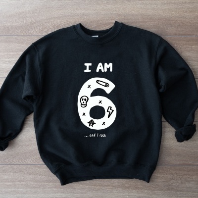 Sweatshirt preta com texto branco I AM 6 ...and I rock em chão de madeira clara