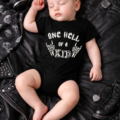 Bebé a dormir vestido com body preto com texto branco e desenhos de mãos esqueléticas, sobre pele preta com acessórios rock
