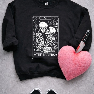 Sweatshirt preta com estampa de esqueletos e coração de peluche rosa com faca espetada