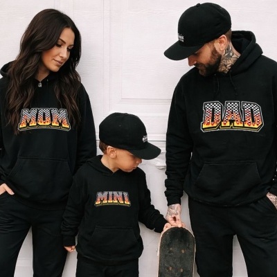 Família com sweats pretas com as palavras MOM, DAD e MINI, criança com skate e boné preto