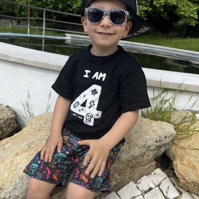 Criança com roupa preta e óculos sentada em pedra junto a água