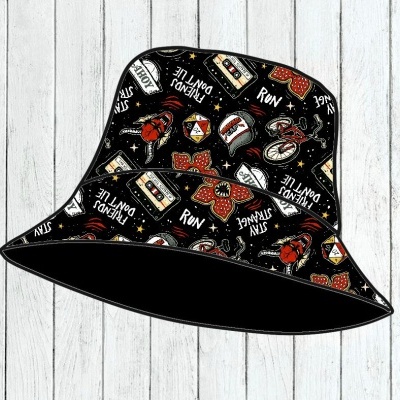 Chapéu bucket preto com diversas estampas coloridas e frases em branco sobre fundo de madeira clara.