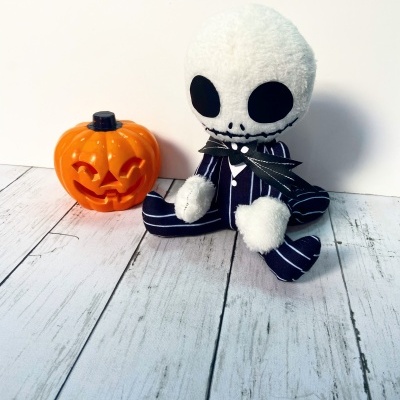 Boneco de peluche com cabeça branca e olhos pretos sentado ao lado de abóbora de plástico laranja