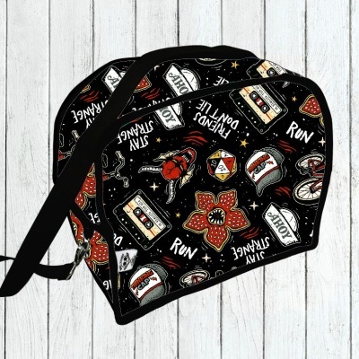 Mala preta com padrão colorido e textos vários sobre fundo de madeira branca.