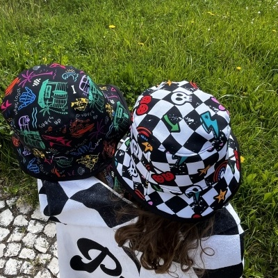 Dois chapéus bucket coloridos usados ao ar livre com relva e calçada de pedras