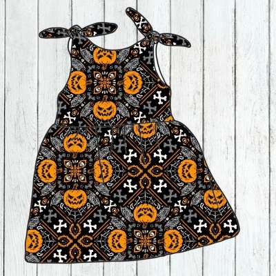 Vestido infantil preto com padrão de abóboras, teias de aranha e cruzes, alças em laço, sobre madeira clara.