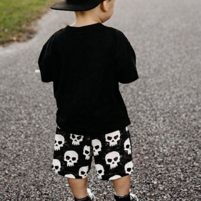 Criança de costas com roupa preta e calções com padrão de caveiras