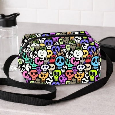 Bolsa tiracolo com padrão colorido de crânios e alça preta sobre bancada cinza