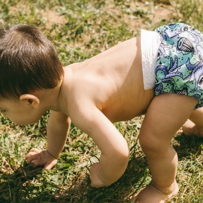 Criança de pele clara de fralda reutilizável colorida a engatinhar na relva
