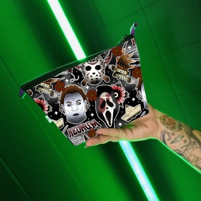 Bolsa de maquilhagem com padrão de personagens de filmes de terror segurada por uma mão tatuada