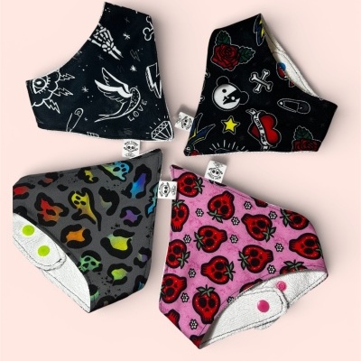 Quatro babetes infantis com padrões coloridos e fechos de pressão, dispostos sobre fundo rosa claro.