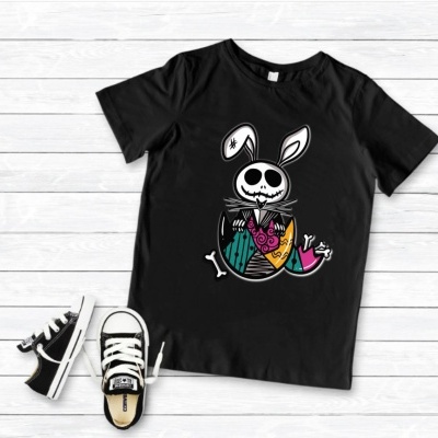 T-shirt preta com estampa de coelho esqueleto e ténis infantis pretos com branco numa superfície de madeira branca